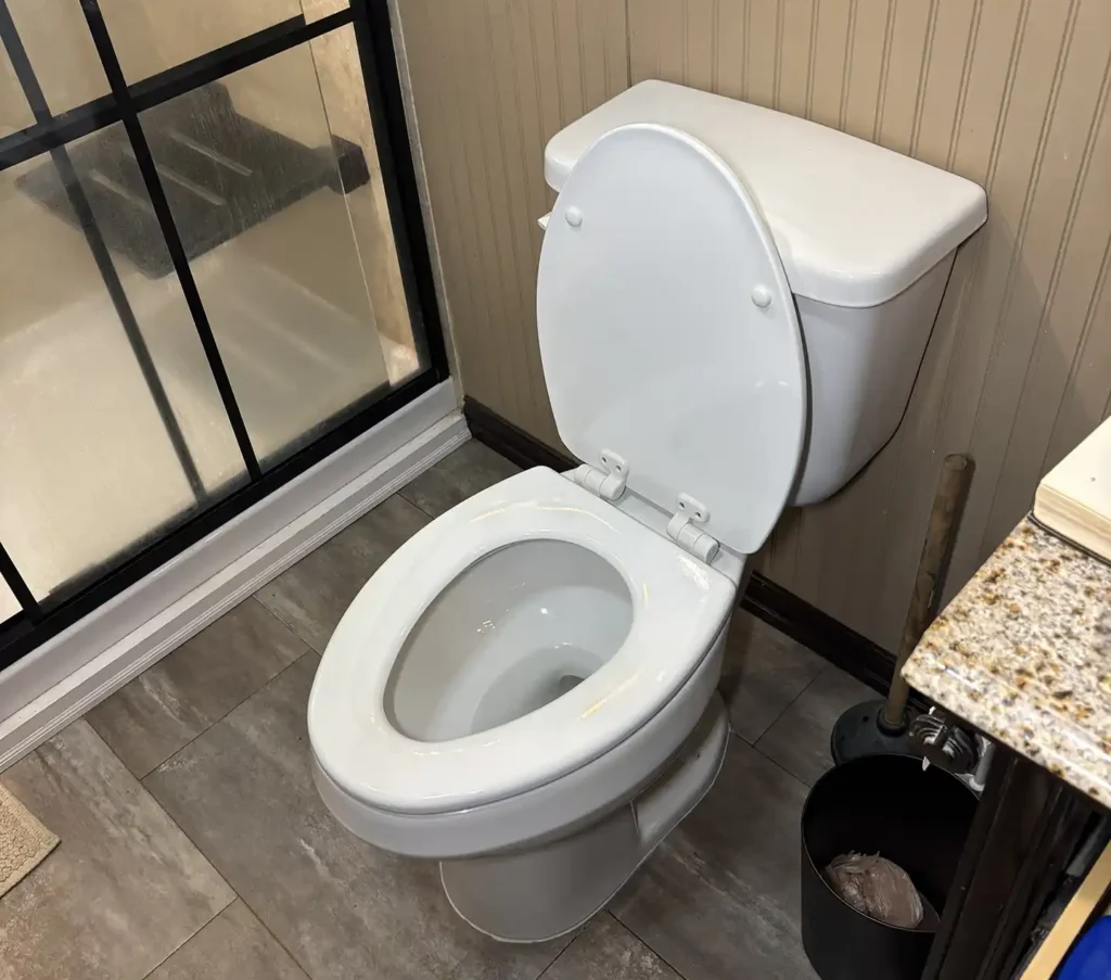 Newly replaced white toilet in bathroom next to glass shower door and tile flooring