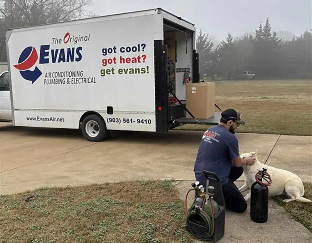 Evans Air technician petting a white dog next to an Evans Air service truck at a residential job